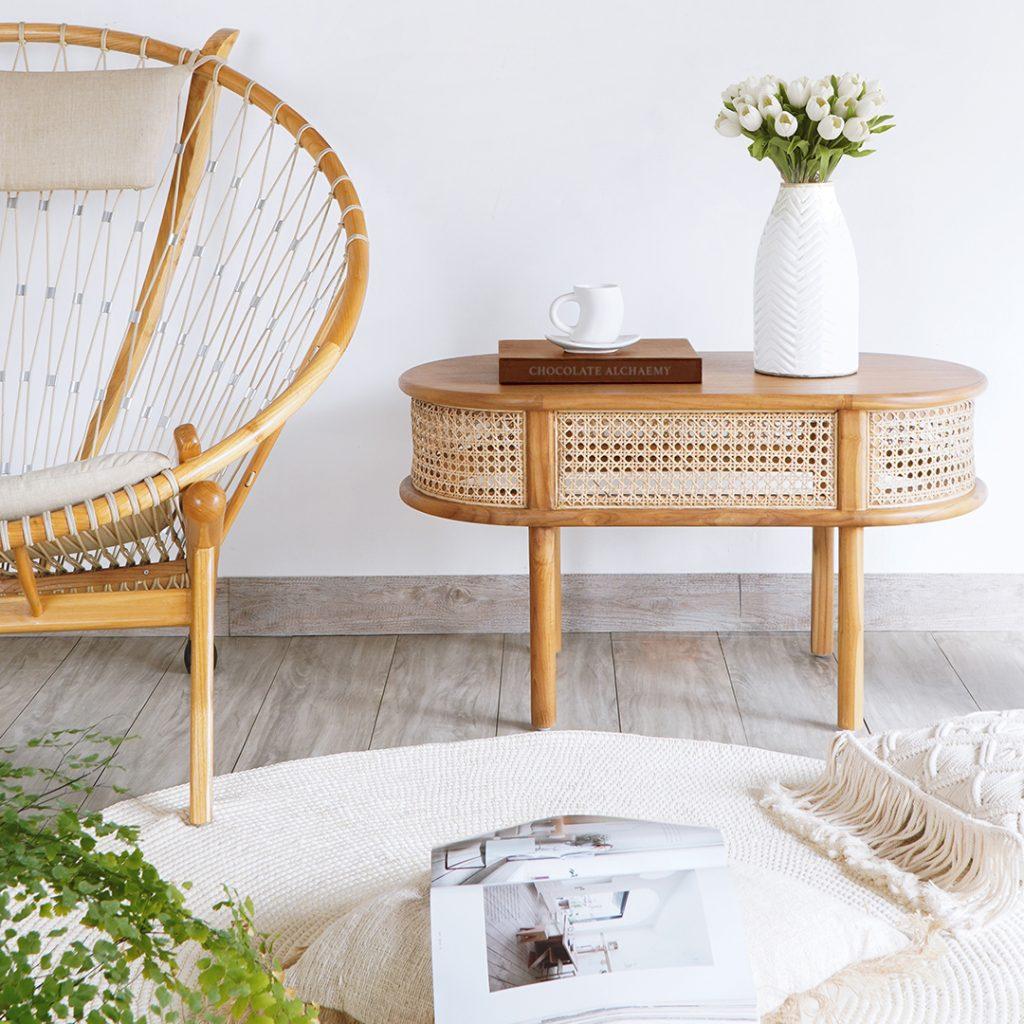 A hoop-back rope armchair beside an oval cane-fronted rattan coffee table with a white vase of tulips and a cup on a book.
