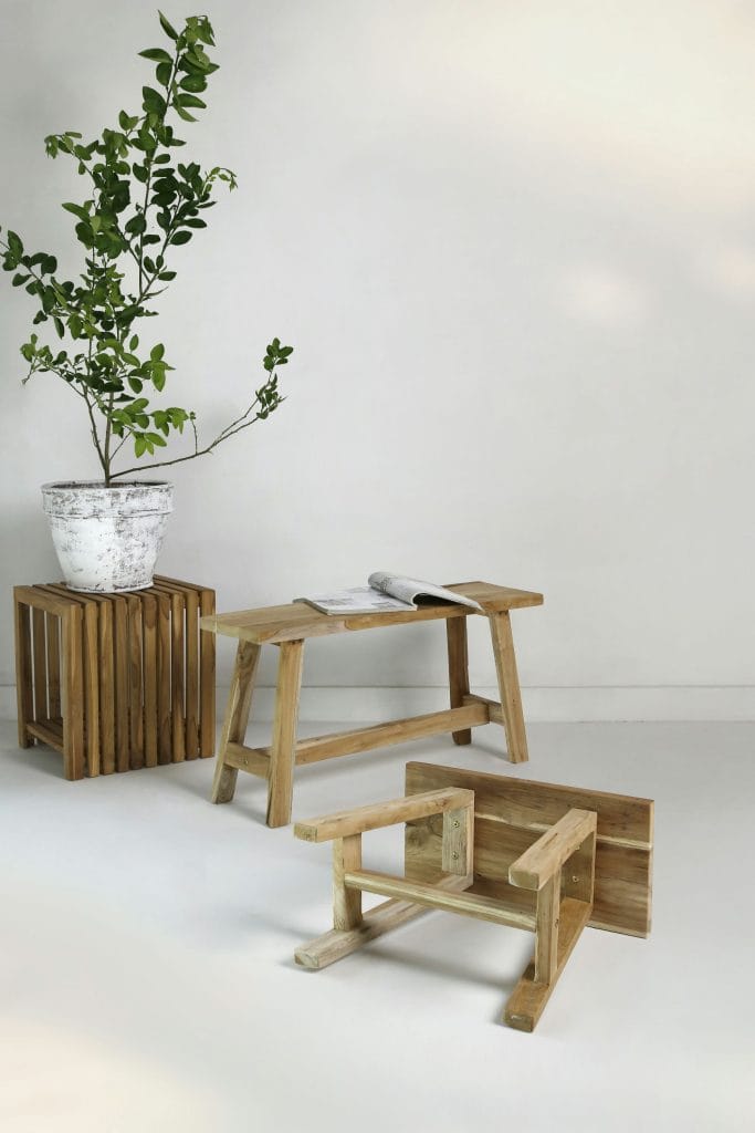 Teak Ranch benches and a slatted teak cube stool beside a potted plant against a white wall.